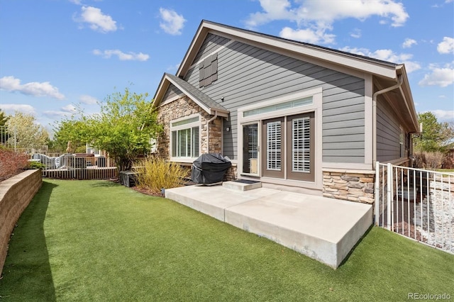 rear view of property with a yard, fence, stone siding, and a patio