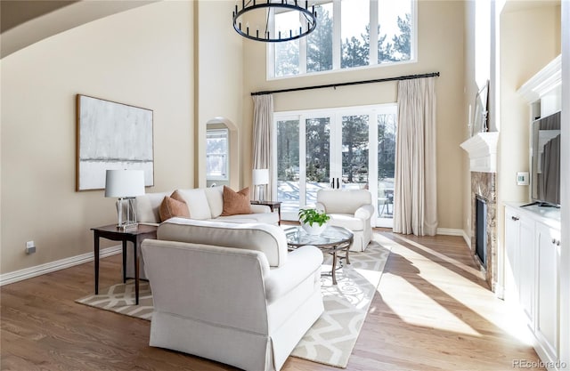 living room featuring an inviting chandelier, a high ceiling, a fireplace, light hardwood / wood-style floors, and french doors