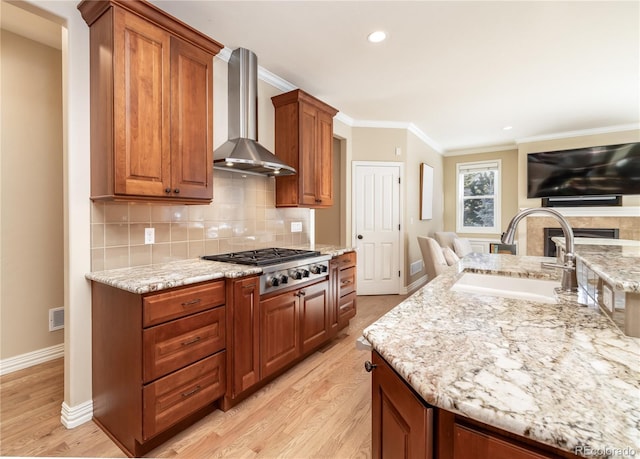 kitchen featuring stainless steel gas stovetop, sink, light stone countertops, wall chimney range hood, and light hardwood / wood-style flooring