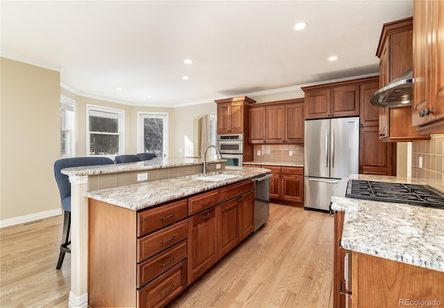 kitchen featuring extractor fan, appliances with stainless steel finishes, a breakfast bar, decorative backsplash, and a large island with sink