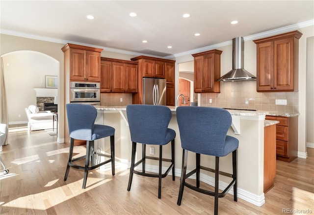 kitchen with appliances with stainless steel finishes, wall chimney exhaust hood, a kitchen island with sink, and backsplash