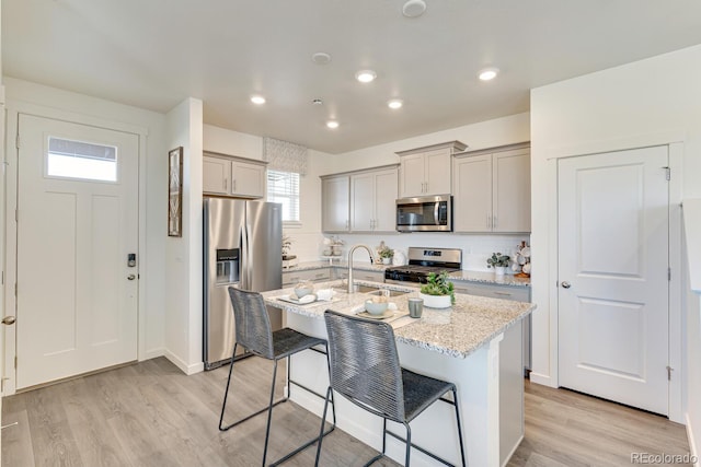 kitchen featuring stainless steel appliances, gray cabinets, light wood-style floors, and a breakfast bar area