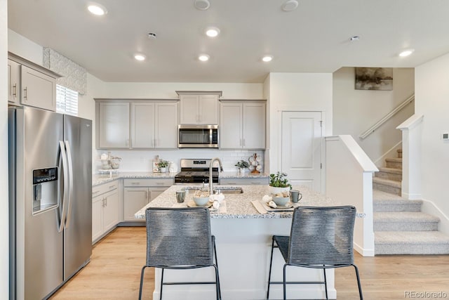 kitchen with light wood finished floors, appliances with stainless steel finishes, a breakfast bar, and light stone counters