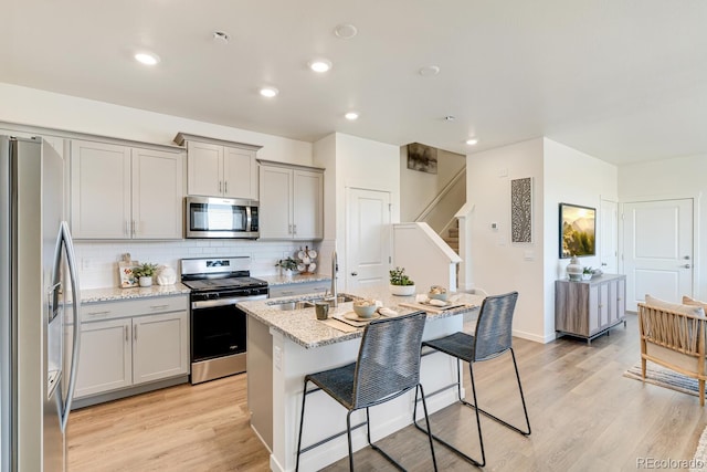 kitchen with a breakfast bar area, stainless steel appliances, a sink, gray cabinets, and backsplash