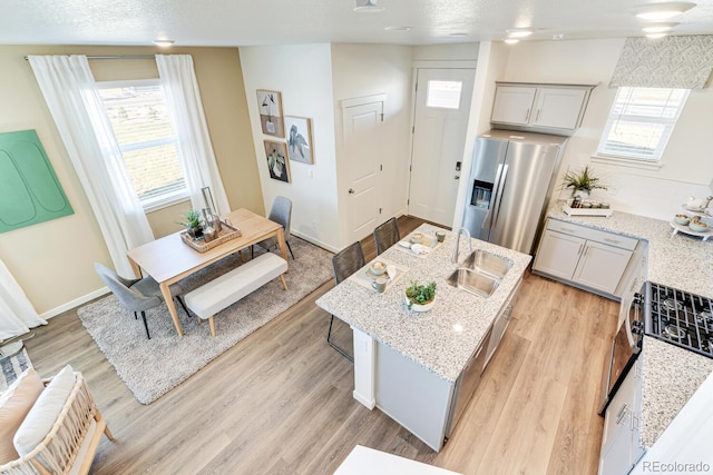 kitchen with light wood-type flooring, light stone countertops, a sink, and stainless steel fridge with ice dispenser