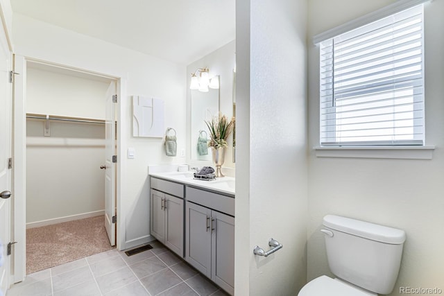 full bathroom featuring double vanity, baseboards, toilet, tile patterned flooring, and a walk in closet