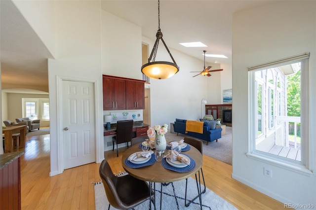 1881 Alma Ln, Superior, CO 80027 - dining space featuring light wood-style flooring, a tile fireplace, a skylight, a ceiling fan, and high vaulted ceiling