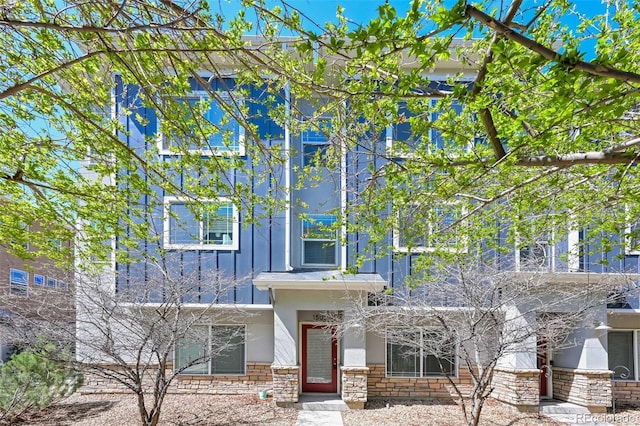 view of front facade with stucco siding, board and batten siding, and stone siding