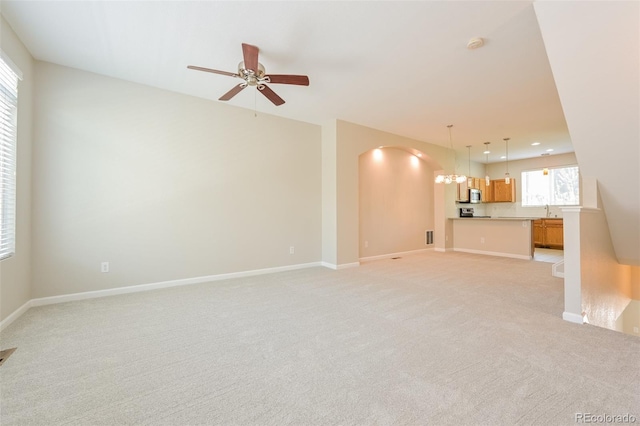 unfurnished living room with ceiling fan with notable chandelier, arched walkways, light carpet, a sink, and baseboards