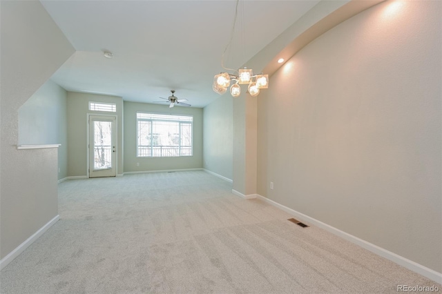 carpeted spare room featuring ceiling fan with notable chandelier, baseboards, and visible vents