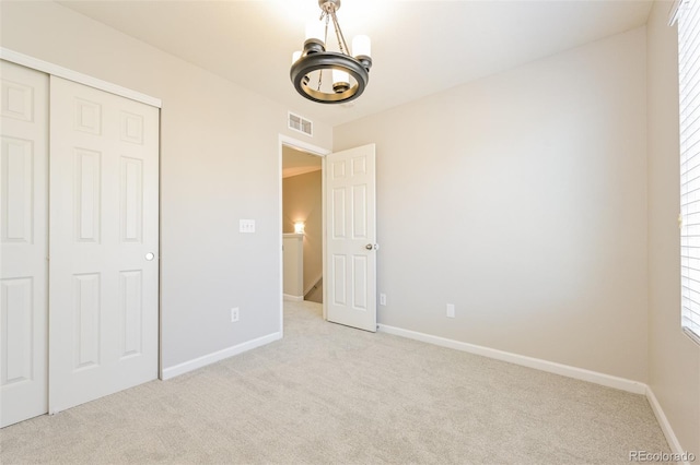 unfurnished bedroom with baseboards, visible vents, light colored carpet, and an inviting chandelier