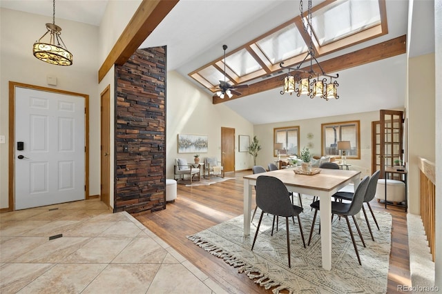dining space with a skylight, high vaulted ceiling, beamed ceiling, and ceiling fan with notable chandelier