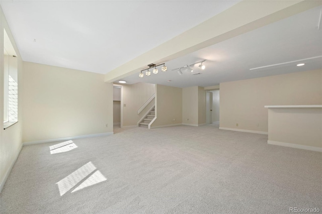 empty room featuring stairs, rail lighting, light colored carpet, and baseboards