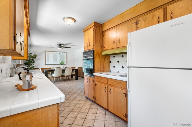7135 S Sherman St, Centennial, CO 80122 - kitchen with freestanding refrigerator, black oven, tile counters, light tile patterned floors, and a ceiling fan