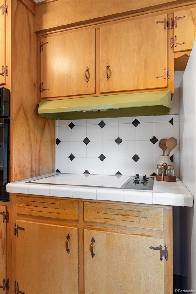 7135 S Sherman St, Centennial, CO 80122 - kitchen with backsplash, under cabinet range hood, brown cabinetry, and black oven