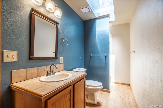 917 Bluebird Ln, Bailey, CO 80421 - bathroom featuring wood finished floors, toilet, vanity, a textured wall, and baseboards