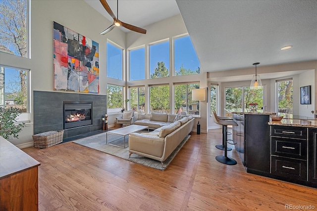 10127 W 100th Ct, Westminster, CO 80021 - living room featuring light wood finished floors, a glass covered fireplace, a ceiling fan, baseboards, and a towering ceiling