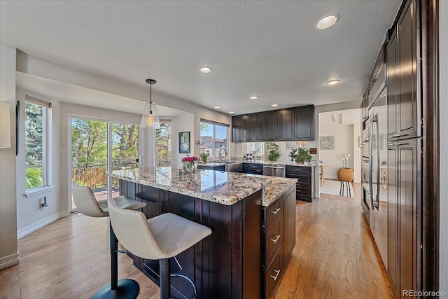 10127 W 100th Ct, Westminster, CO 80021 - kitchen with stainless steel dishwasher, a center island, light wood-style floors, light stone counters, and a breakfast bar area