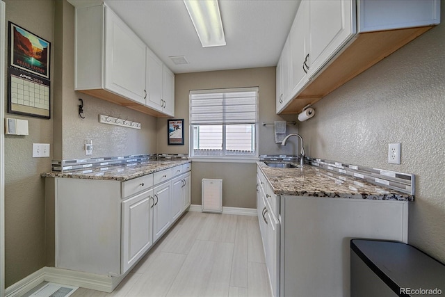10127 W 100th Ct, Westminster, CO 80021 - kitchen featuring a sink, baseboards, white cabinets, light stone counters, and a textured wall
