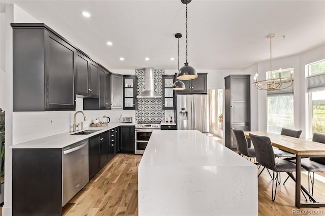 1588 W 111th Ave, Northglenn, CO 80234 - kitchen featuring wall chimney range hood, appliances with stainless steel finishes, a chandelier, a kitchen island, and decorative backsplash