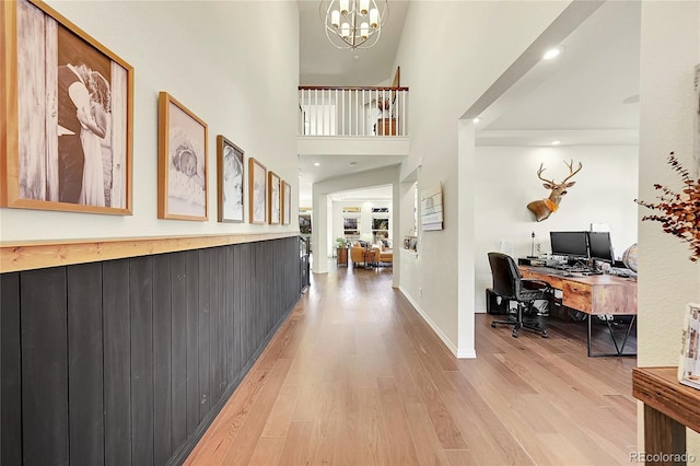 hallway with a high ceiling, a notable chandelier, and light hardwood / wood-style floors