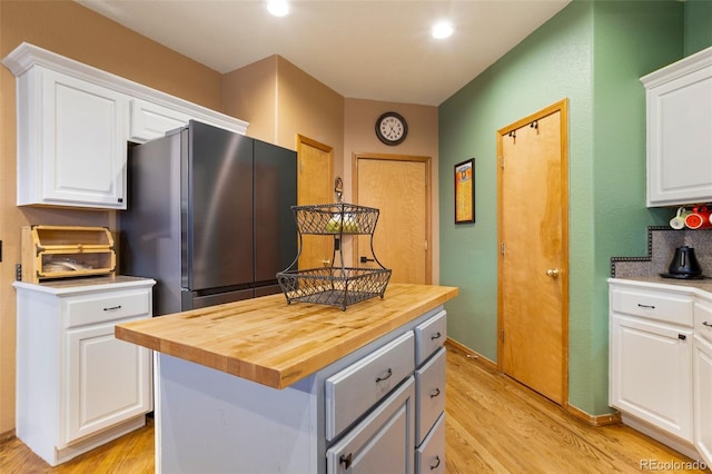 kitchen featuring stainless steel fridge, white cabinetry, light wood-type flooring, and a kitchen island