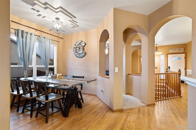 dining area with light hardwood / wood-style flooring, a notable chandelier, and a textured ceiling