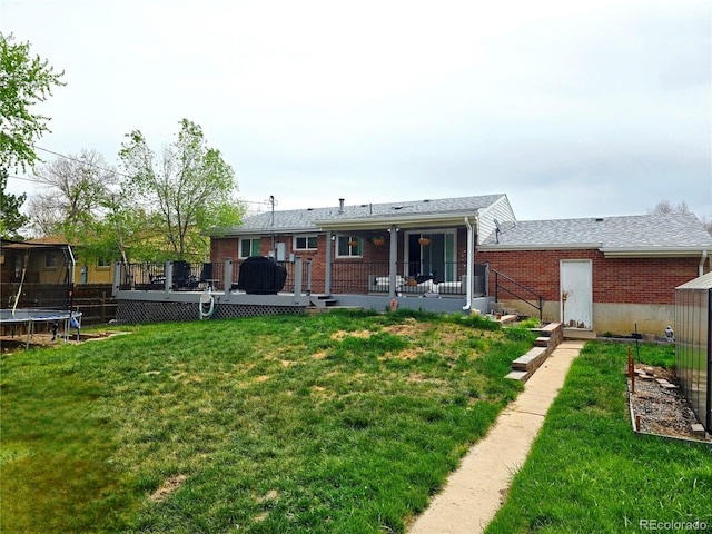 465 Salem St, Aurora, CO 80011 - rear view of house with a trampoline, a wooden deck, a lawn, and brick siding