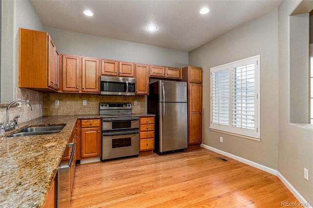 kitchen with light wood finished floors, appliances with stainless steel finishes, decorative backsplash, and a sink