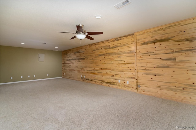 spare room with carpet, visible vents, ceiling fan, and wooden walls