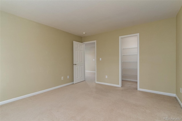 unfurnished bedroom with a closet, a walk in closet, light colored carpet, and baseboards