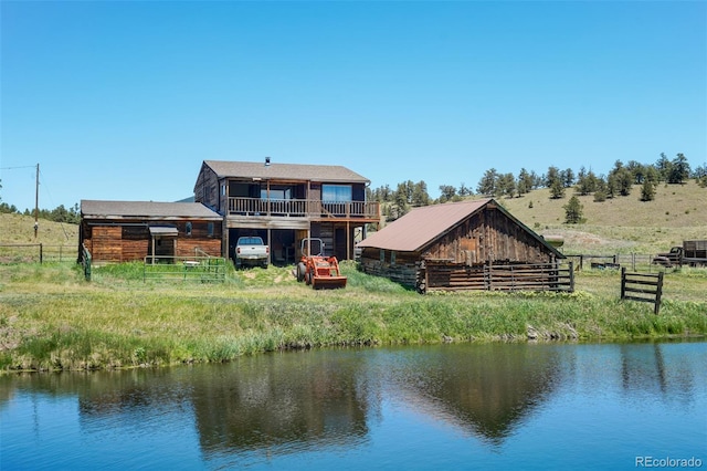 back of house with a rural view, an outbuilding, and a water view