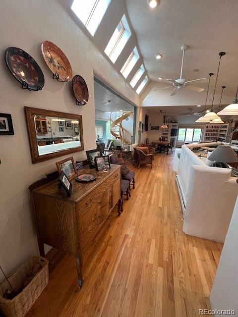 interior space featuring ceiling fan, lofted ceiling with skylight, and light hardwood / wood-style floors