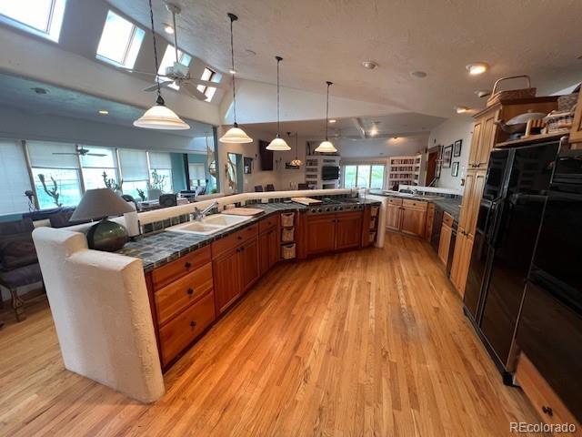 kitchen with decorative light fixtures, light hardwood / wood-style floors, high vaulted ceiling, kitchen peninsula, and ceiling fan