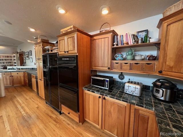 kitchen with light hardwood / wood-style floors, tile counters, and black appliances