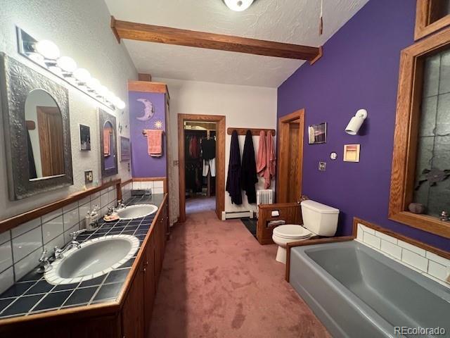 bathroom with beam ceiling, toilet, dual bowl vanity, and a tub to relax in