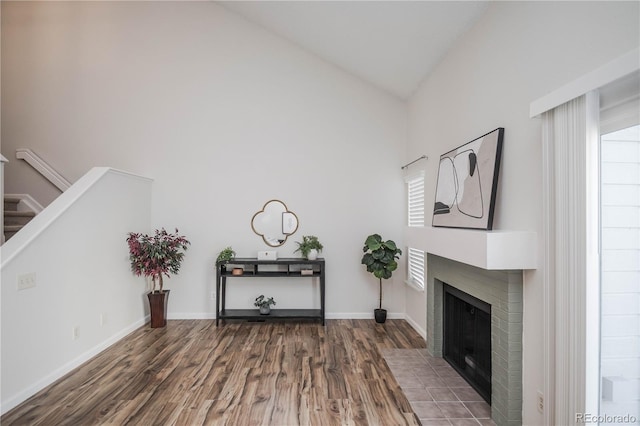 sitting room with hardwood / wood-style flooring, high vaulted ceiling, and a brick fireplace