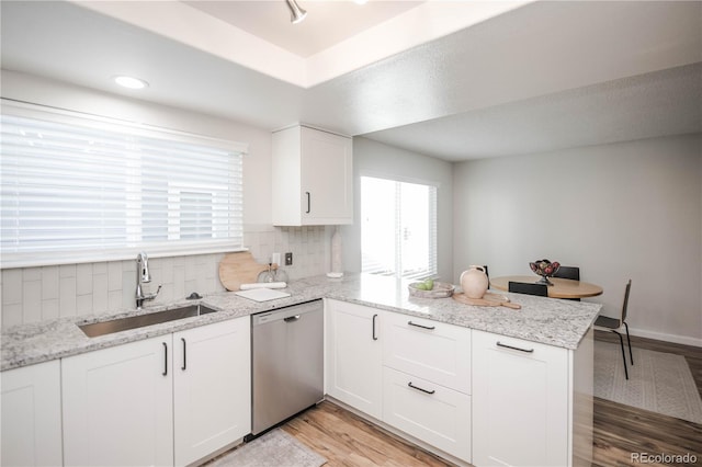 kitchen with light hardwood / wood-style flooring, dishwasher, kitchen peninsula, light stone countertops, and white cabinets