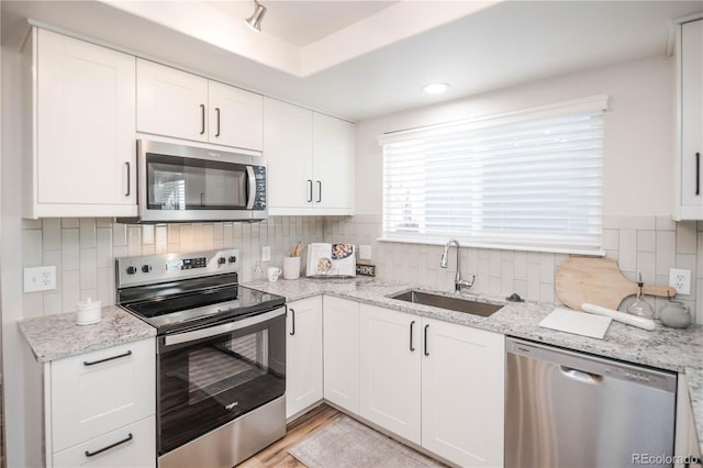 kitchen with appliances with stainless steel finishes, sink, white cabinets, and light stone counters