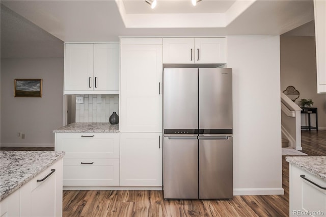 kitchen featuring wood-type flooring, white cabinets, stainless steel fridge, light stone counters, and a tray ceiling