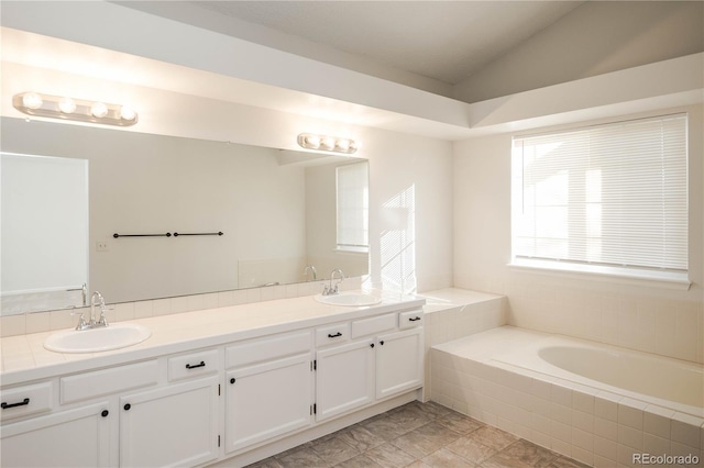 bathroom with vanity, tiled bath, and vaulted ceiling