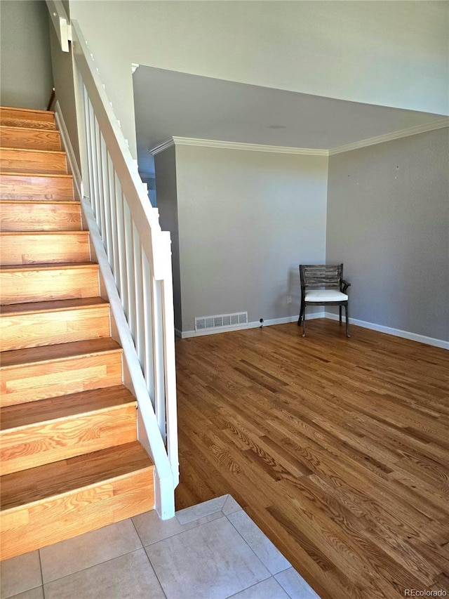 stairs with ornamental molding, wood finished floors, visible vents, and baseboards