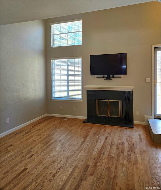 unfurnished living room with baseboards, wood finished floors, and a glass covered fireplace