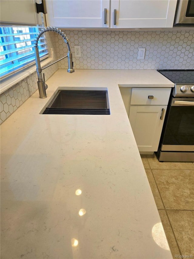 room details with a sink, stainless steel electric range oven, decorative backsplash, and white cabinetry
