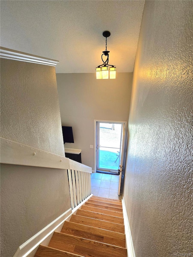 stairway with baseboards, wood finished floors, and a textured wall