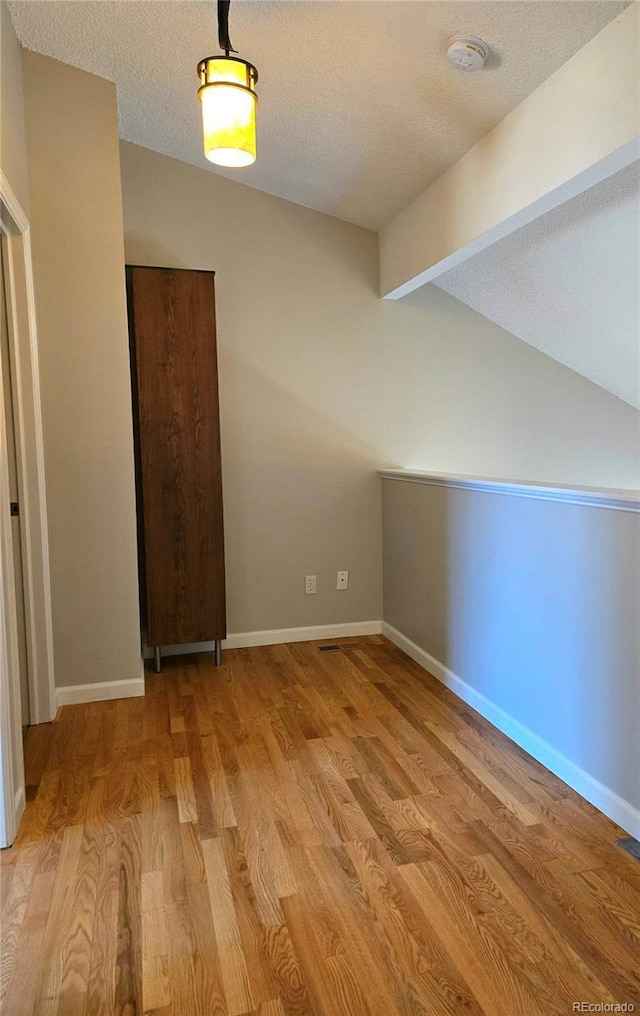 spare room with baseboards, light wood-style flooring, lofted ceiling with beams, and a textured ceiling