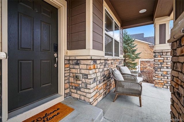 view of exterior entry featuring stone siding and covered porch