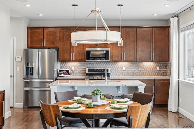 kitchen with dark wood finished floors, an island with sink, tasteful backsplash, and stainless steel appliances
