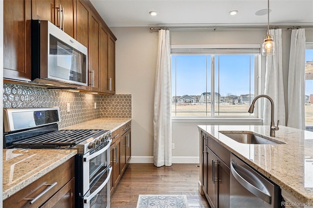 kitchen featuring decorative backsplash, dark wood-style flooring, light stone countertops, stainless steel appliances, and a sink