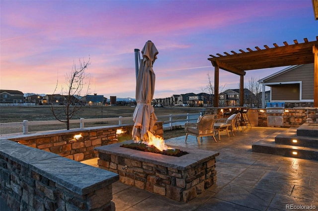 view of patio with exterior kitchen, fence, a grill, a fire pit, and a pergola